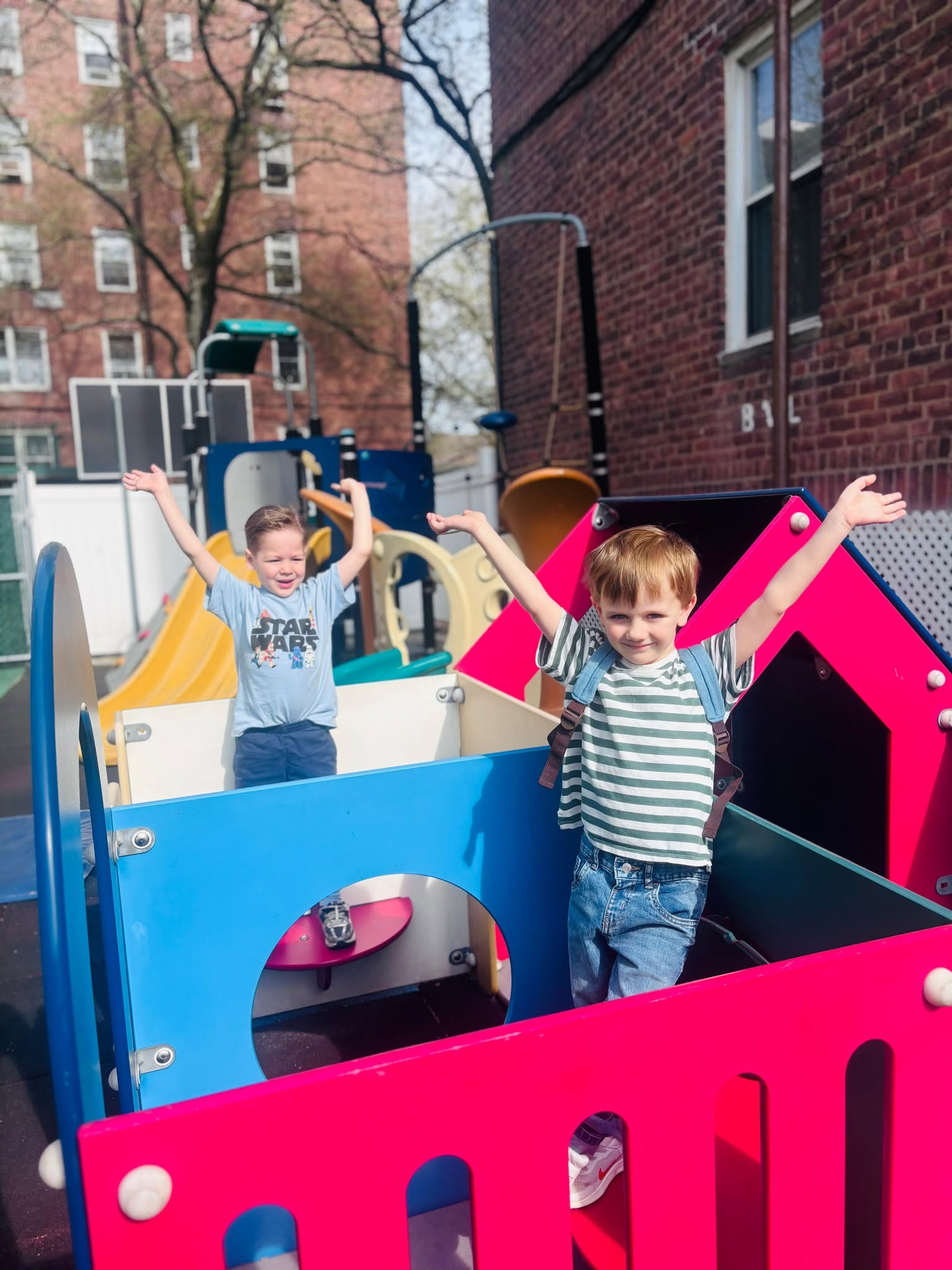 Two children cheering with arms raised on colorful playground equipment