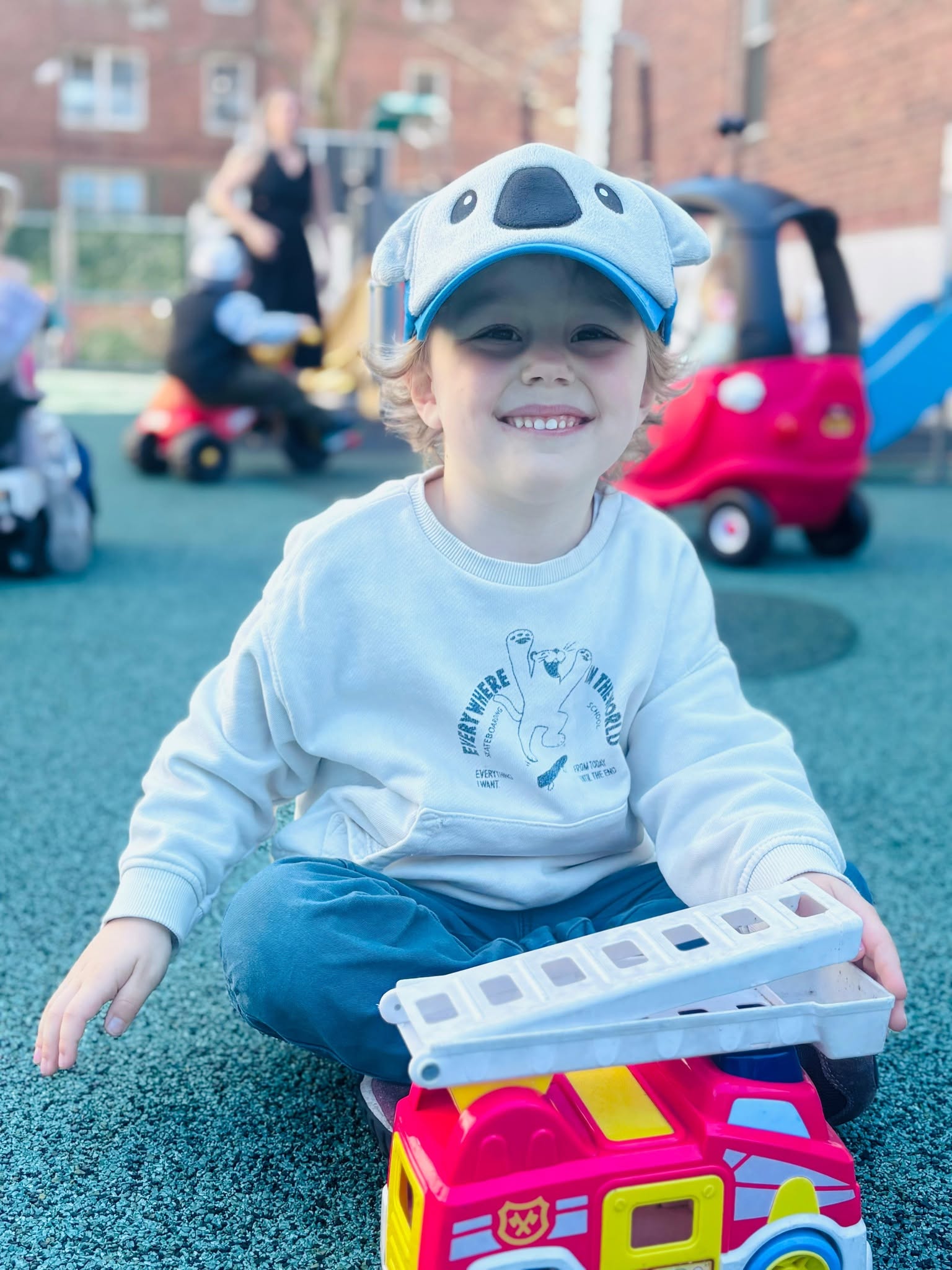 Smiling child playing with a toy fire truck on the play surface