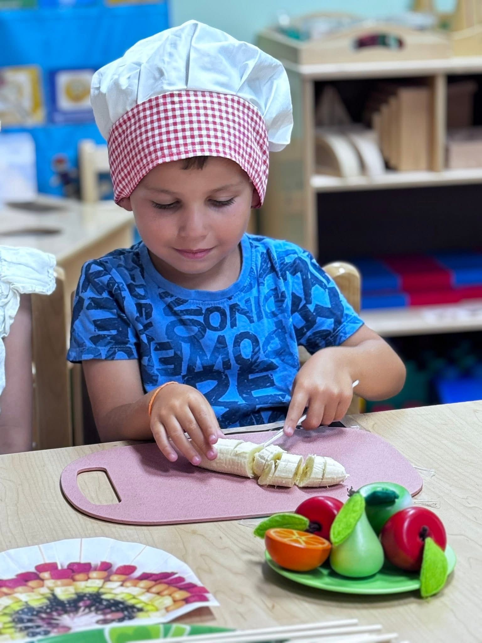 Boy in a chef hat carefully slicing a banana