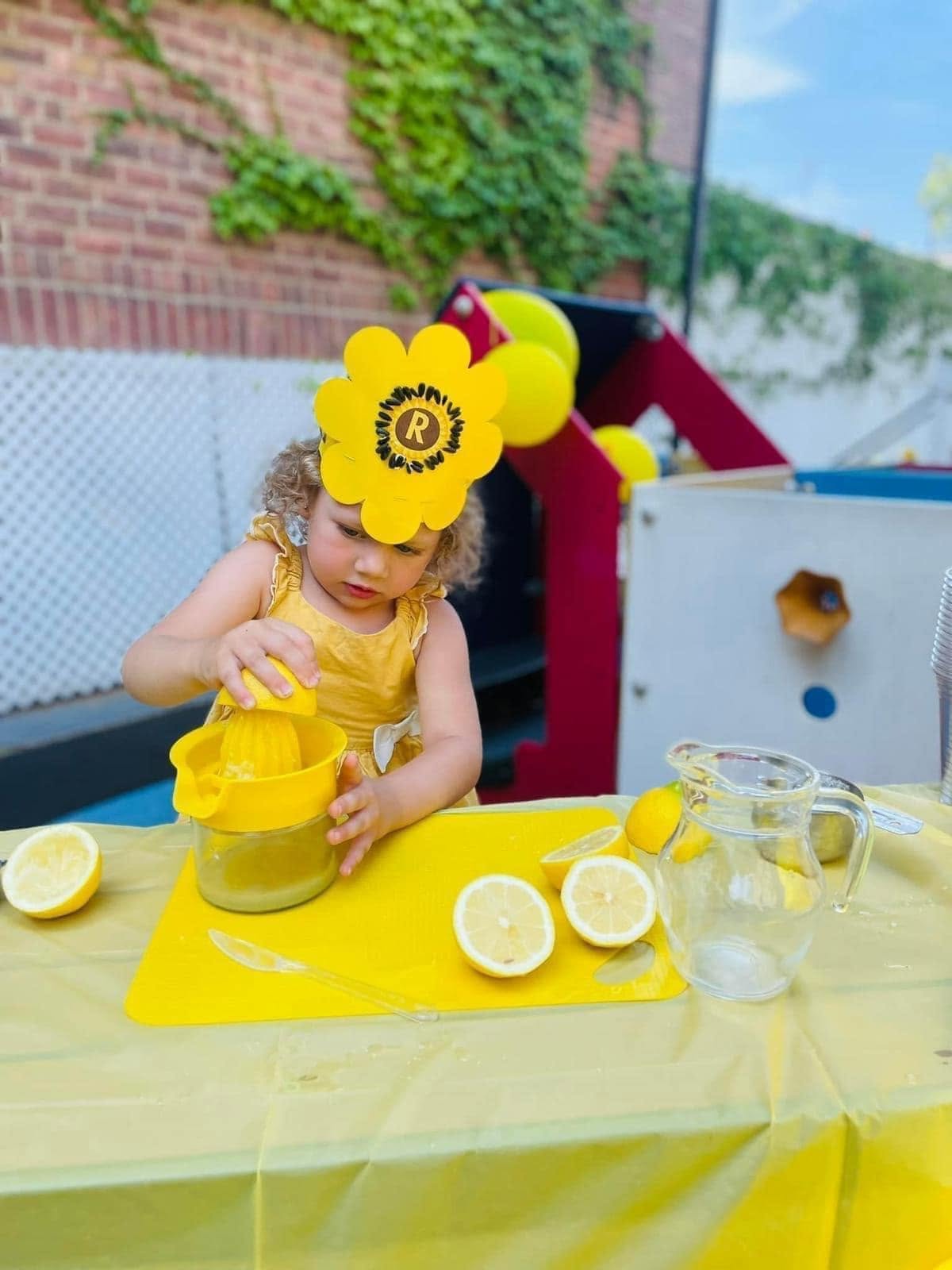Girl in a flower hat squeezing lemons at a lemonade stand